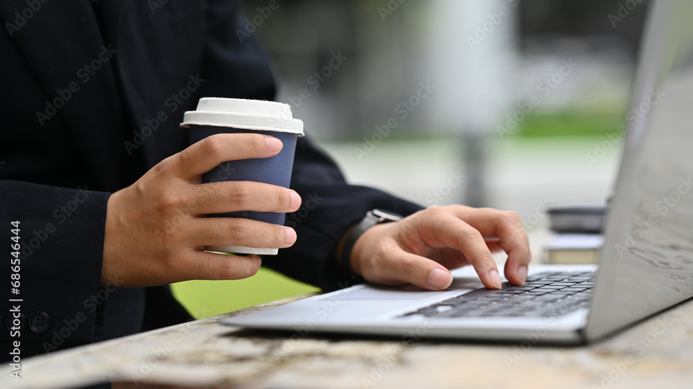 Cropped shot businesswoman with take away coffee cup using laptop at outdoor
