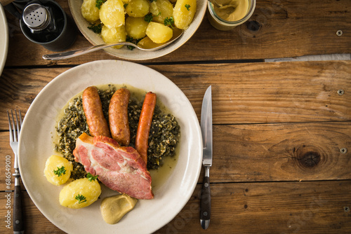 Oldenburger Grünkohl mit geräucherter Kohlwurst, Pinkel, Kassler Nacken, Kartoffeln, Senf, Petersilie auf Teller und Holz Hintergrund