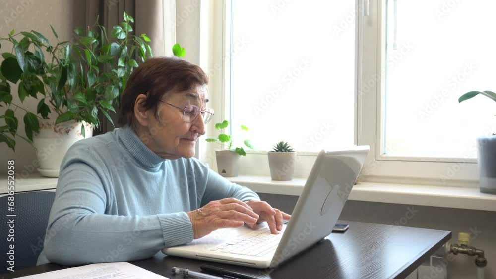 Grandmother works on the computer at home. He presses his fingers on the keyboard and looks at the screen. The concept of active aging, activities in older age, computer literacy for pensioners. Grandmother works on the computer at home. He presses his fingers on the keyboard and looks at the screen. The concept of active aging, activities in older age, computer literacy for pensioners.