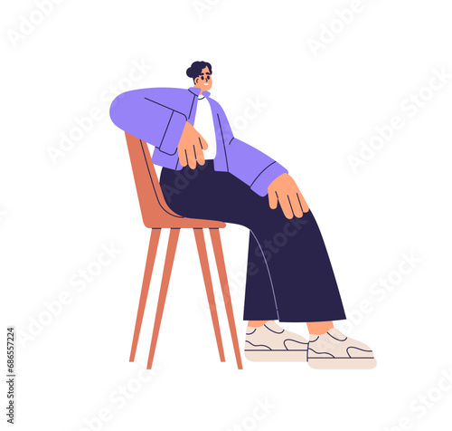 Young smiling man sitting in chair, leaning on chairback, posing. Male charac...