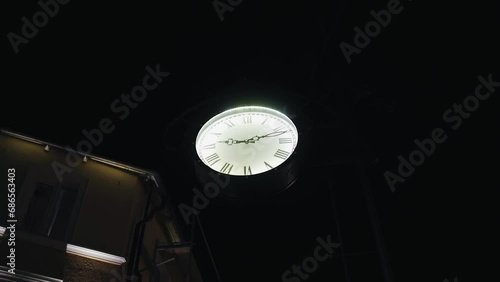The clock is hanging on a pole on the night street. Shooting a watch in motion photo