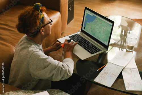 Side view of elderly woman planning trip on map in laptop at home photo