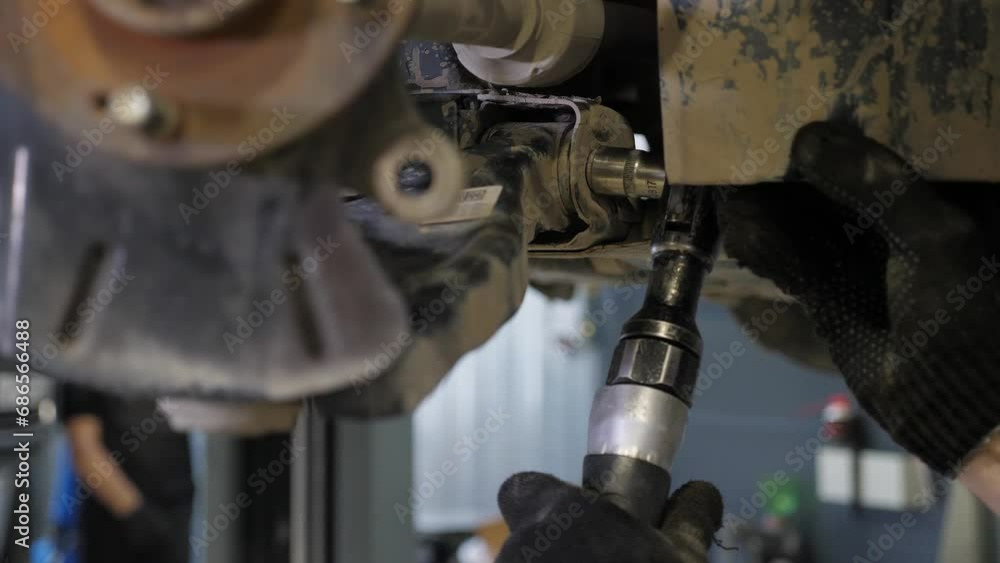 A close-up of an auto mechanic repairing brake pads on a car wheel at a service station, he uses a wrench. An auto mechanic repairs a car in an auto repair shop. A close-up of an auto mechanic repairing brake pads on a car wheel at a service station, he uses a wrench. An auto mechanic repairs a car in an auto repair shop.
