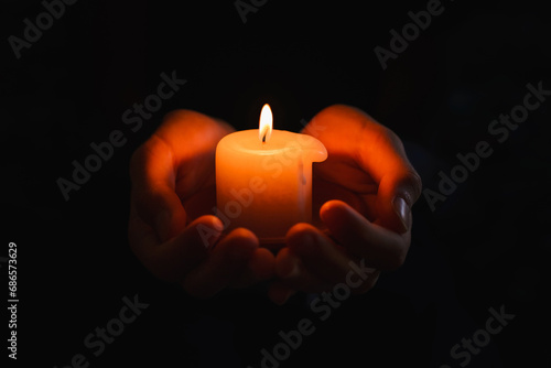 boy holds in a hand a burning candle against black background.Religious concept.