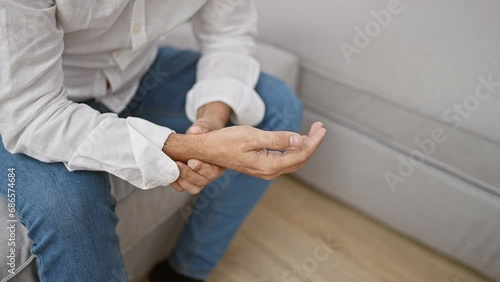 Worried young hispanic man with grey hair, enduring wrist pain at home, sitting unhappily on his living room sofa photo