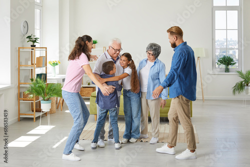 Full length portrait of happy jouful smiling big family of parents, grandparents and children standing in the living room at home. Kids hugging their grandfather. Family leisure concept.