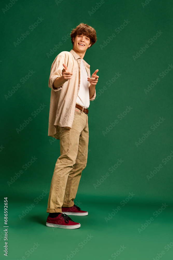 Full-length portrait of young successful, motivated man points to camera and say that you can do everything against green studio background.