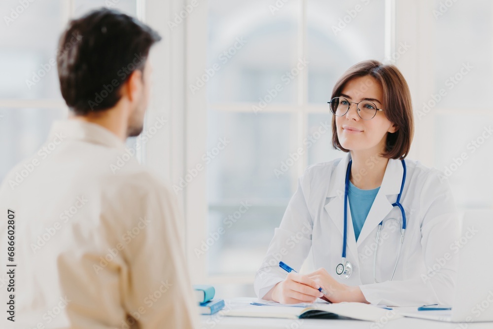 Female doctor consulting with male patient in a well-lit medical office Female doctor consulting with male patient in a well-lit medical office