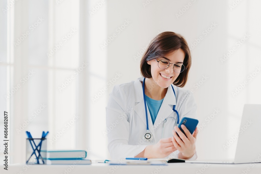 Smiling female doctor using smartphone in a well-lit medical office setting Smiling female doctor using smartphone in a well-lit medical office setting