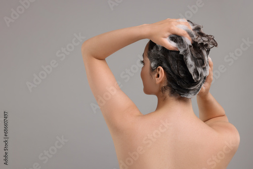 Woman washing hair on grey background, back view. Space for text
