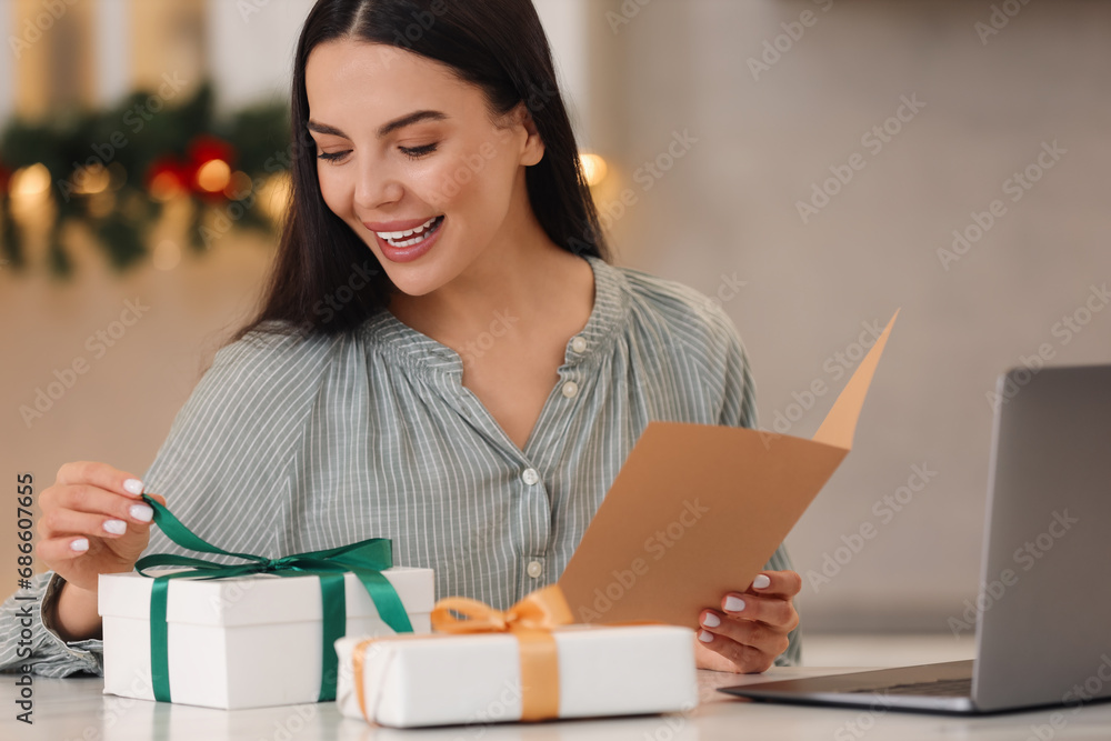 Celebrating Christmas online with exchanged by mail presents. Smiling woman opening gift box during video call on laptop at home Celebrating Christmas online with exchanged by mail presents. Smiling woman opening gift box during video call on laptop at home