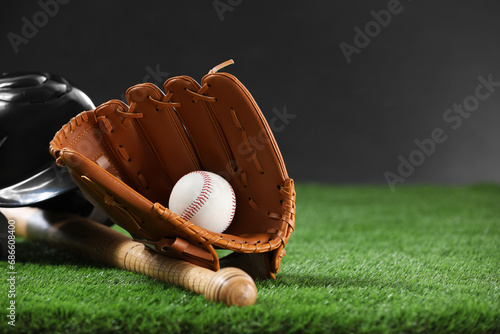 Baseball bat, batting helmet, leather glove and ball on green grass against dark background. Space for text