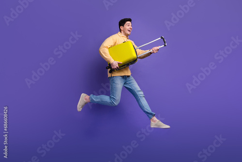 Full length photo of handsome young guy running hold baggage adventure wear trendy yellow garment isolated on violet color background