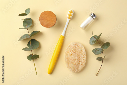 Plastic toothbrush, eucalyptus branches and other toiletries on pale yellow background, flat lay