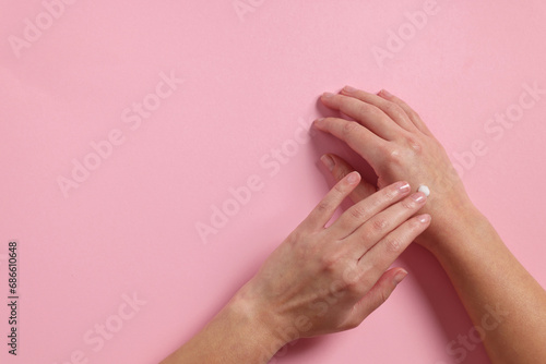 Woman applying cosmetic cream onto hand on pink background, top view. Space for text