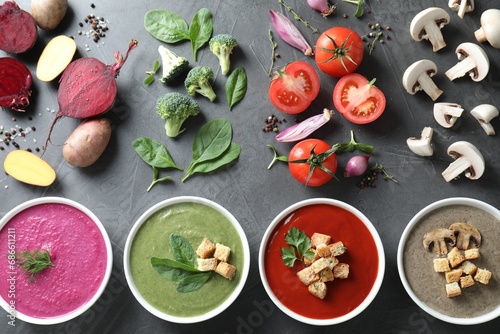 Different tasty cream soups in bowls and ingredients on dark grey table, flat lay
