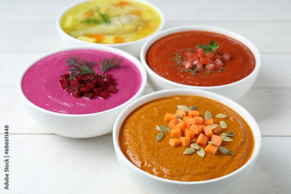 Tasty broth and different cream soups in bowls on white wooden table, closeup Tasty broth and different cream soups in bowls on white wooden table, closeup