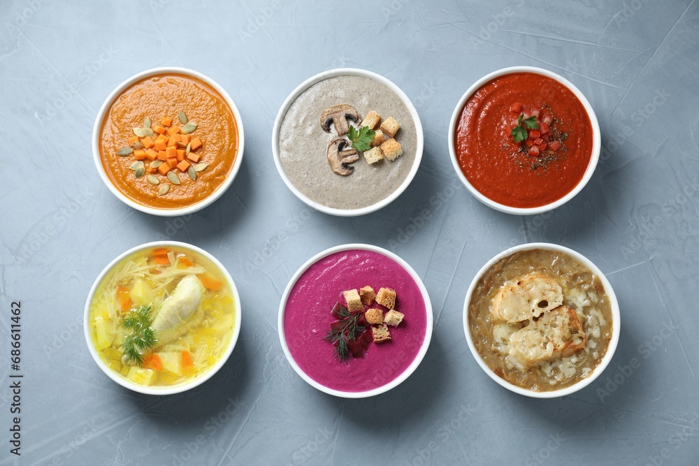 Tasty broth and different cream soups in bowls on gray table, flat lay Tasty broth and different cream soups in bowls on gray table, flat lay