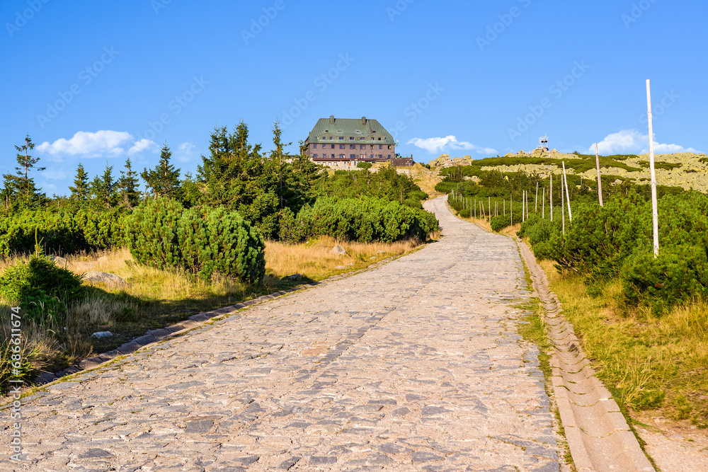 Karkonosze Mountains, Szrenica shelter in the Western Sudetes, a wide mountain trail leading to the shelter, mountain landscape with high-mountain vegetation on a sunny summer day.