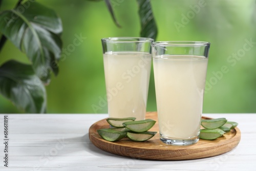 Fresh aloe juice in glasses and cut leaves on white wooden table outdoors. Space for text