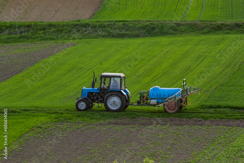 Aerial view of tractor spraying crop in green farm fields with pesticide