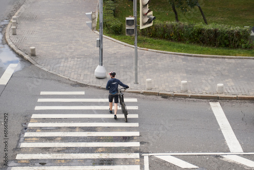 Man crosses the road at a pedestrian crossing and carries a bicycle next to him. View from above.