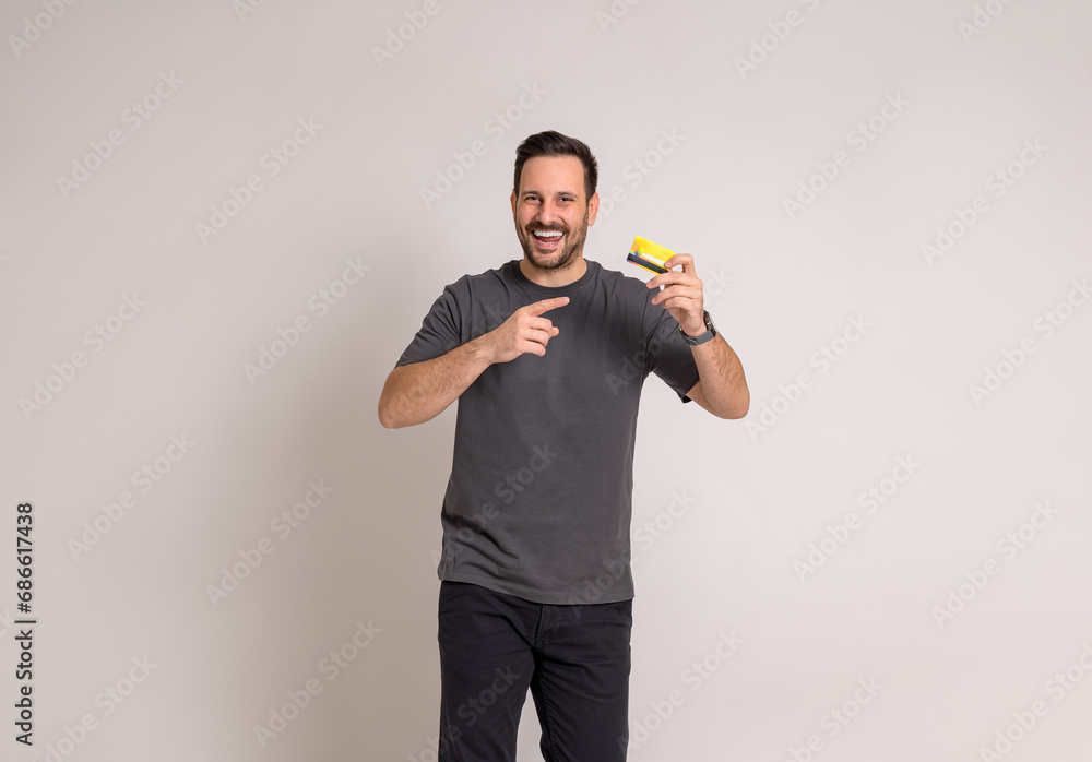 Cheerful young businessman laughing and pointing at credit card while standing on white background Cheerful young businessman laughing and pointing at credit card while standing on white background