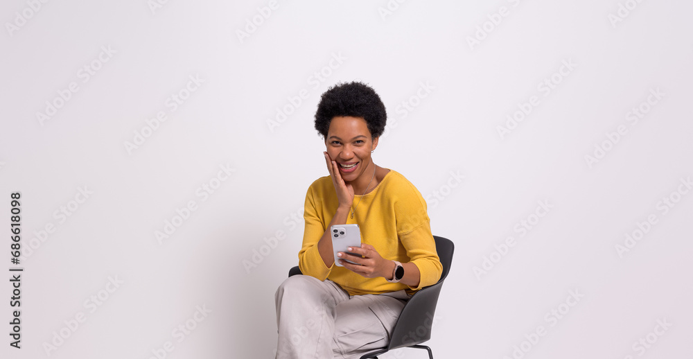 Happy businesswoman with hand on chin messaging over smartphone on chair against white background Happy businesswoman with hand on chin messaging over smartphone on chair against white background