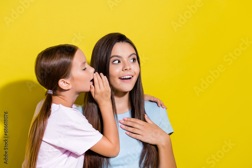 Photo of adorable cheerful small siblings dressed t-shirts telling rumors looking empty space isolated yellow color background