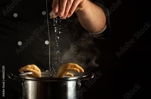 Fotografie The cook pours salt into a pan with boiling chicken legs