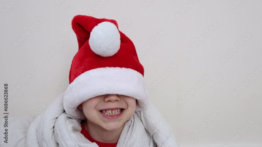 adorable cute kid boy with santa claus cap or christmas tree,reindeer horns as headband is having fun getting crazy,isolated.child preschooler wrapped in cozy warm blanket on bed.laughing boy adorable cute kid boy with santa claus cap or christmas tree,reindeer horns as headband is having fun getting crazy,isolated.child preschooler wrapped in cozy warm blanket on bed.laughing boy