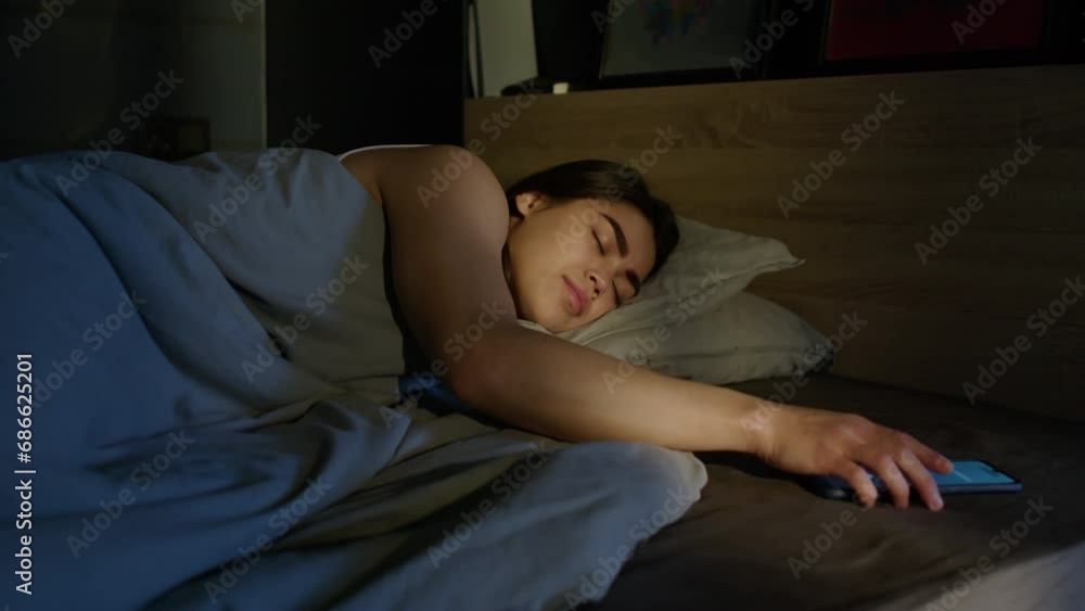 Young woman taking phone to turn off alarm while waking up in morning Young woman taking phone to turn off alarm while waking up in morning