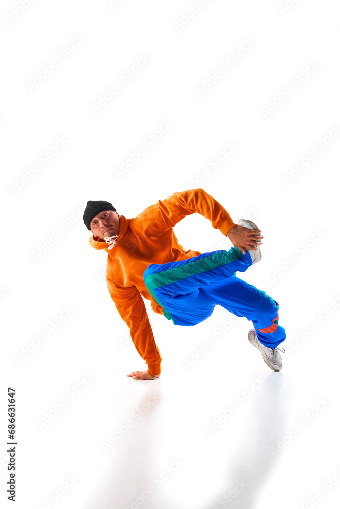 Stylishly dressed man, guy, professional dancer training breakdance freezes, flexing in dace hall in motion against white background.