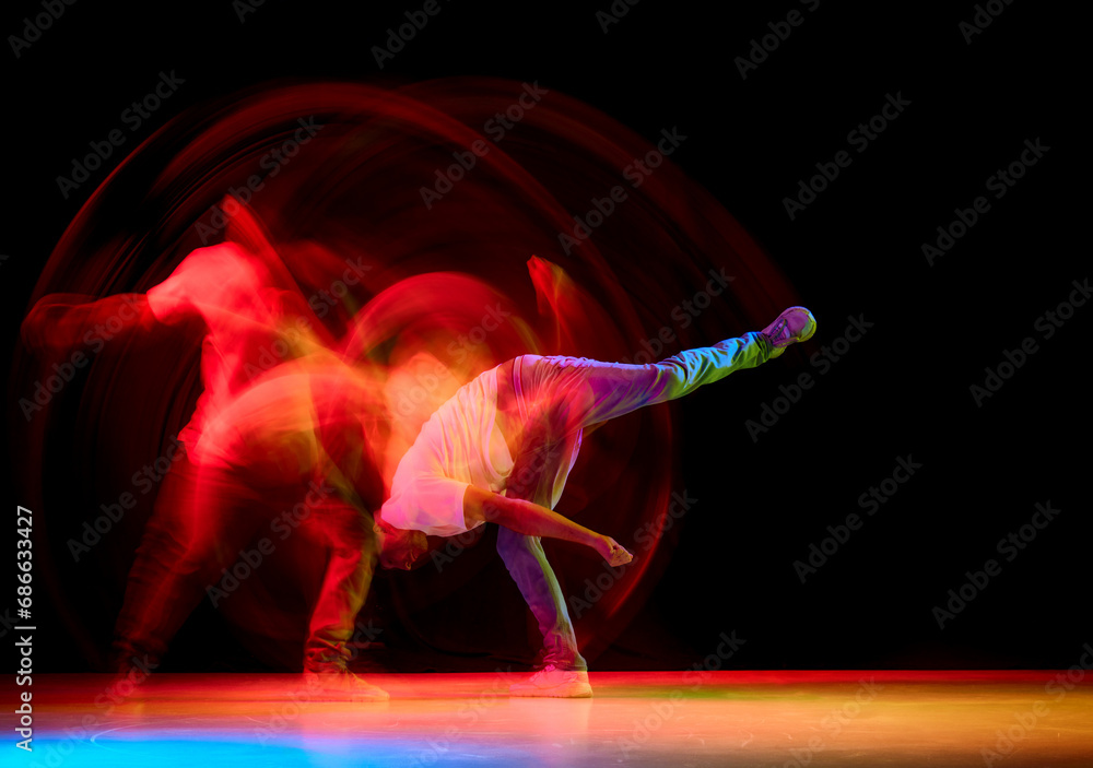 Young sportive guy dancing hip-hop, breakdance against black studio studio background in red neon light with motion blur.