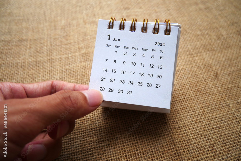 Hand holding a desk calendar of January 2024 years on pink background ...