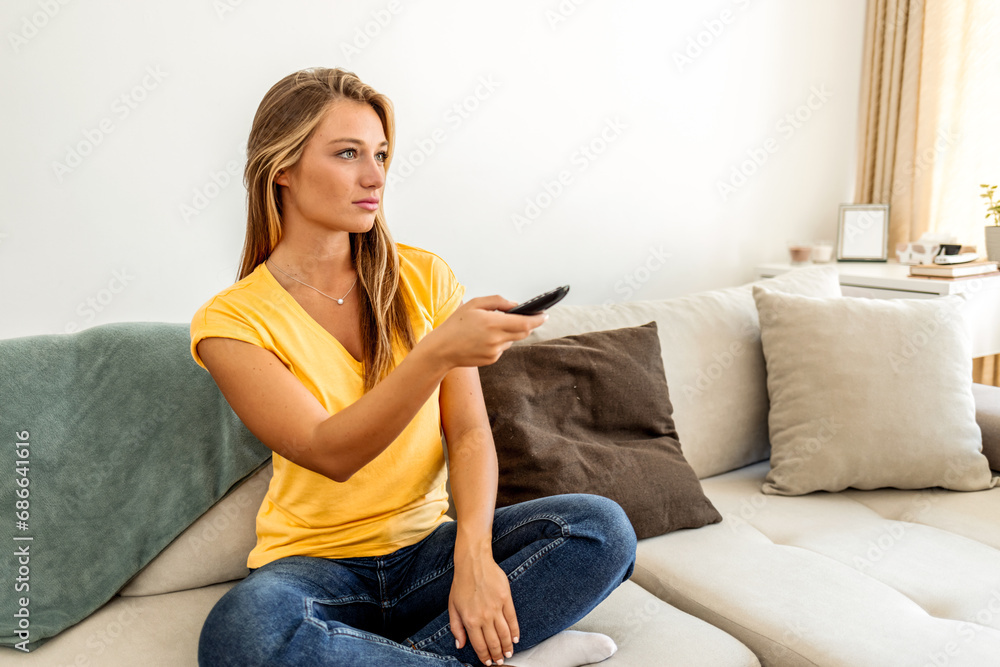 Shot of a young woman holding a remote control while sitting on the sofa at home.