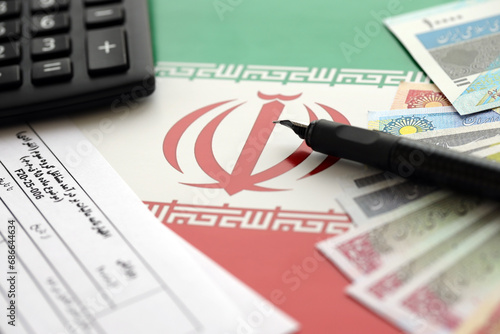 Iranian annual income tax return form F20-25-006 ready to fill on table with pen, calculator and iranian money on flag close up photo