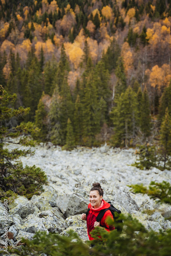 A girl with a backpack climbs a hill, a tourist route in an autumn forest, trekking in the mountains, outdoor recreation.