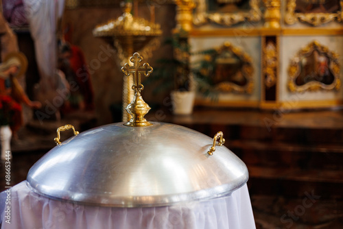 Aluminium church font, large bowl, with golden cross and saint water for the baptism of babies in Orthodox Church temple, Christening ceremony.Concept of rituals, sacraments of the Christian religion.