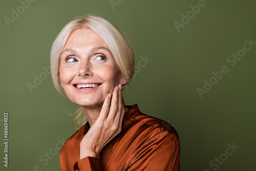 Photo portrait of lovely senior lady touch cheek look empty space wear trendy satin brown garment isolated on khaki color background photo