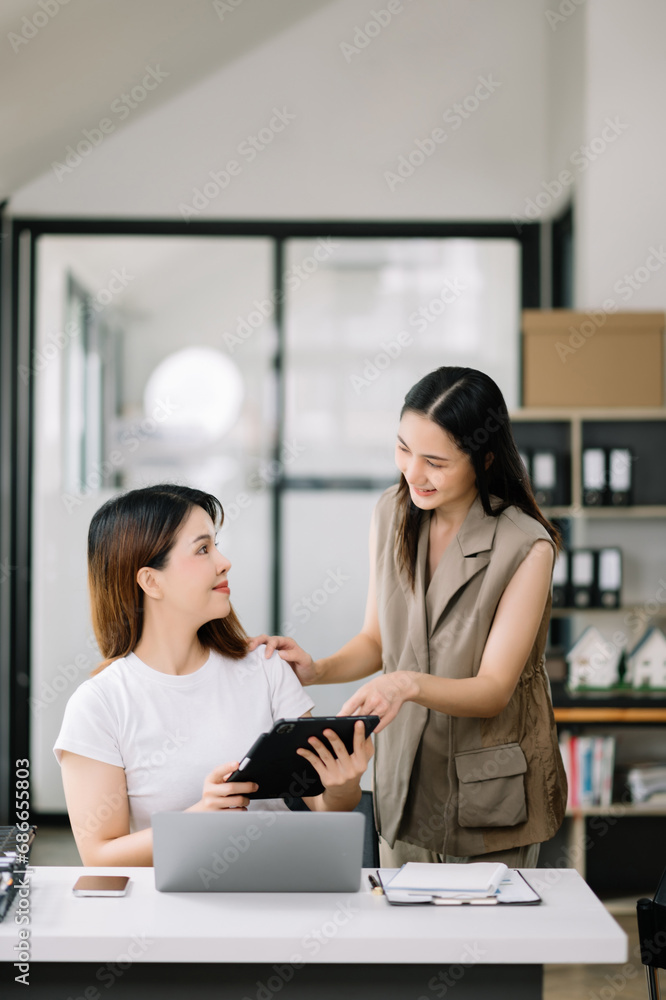 Two Asian businesswoman discuss investment project working and planning strategy with tablet laptop computer Two Asian businesswoman discuss investment project working and planning strategy with tablet laptop computer