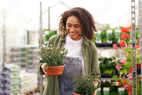 Smiling woman gardener holding flower pot while standing on greenhouse yard background photo