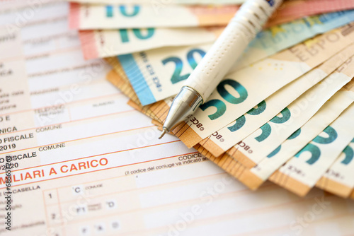 Filling italian tax form process with pen and euro money bills close up. Tax paying period and deadline