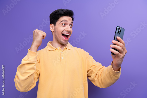 Photo of excited lucky man dressed yellow shirt winning game modern device rising fist isolated purple color background © deagreez