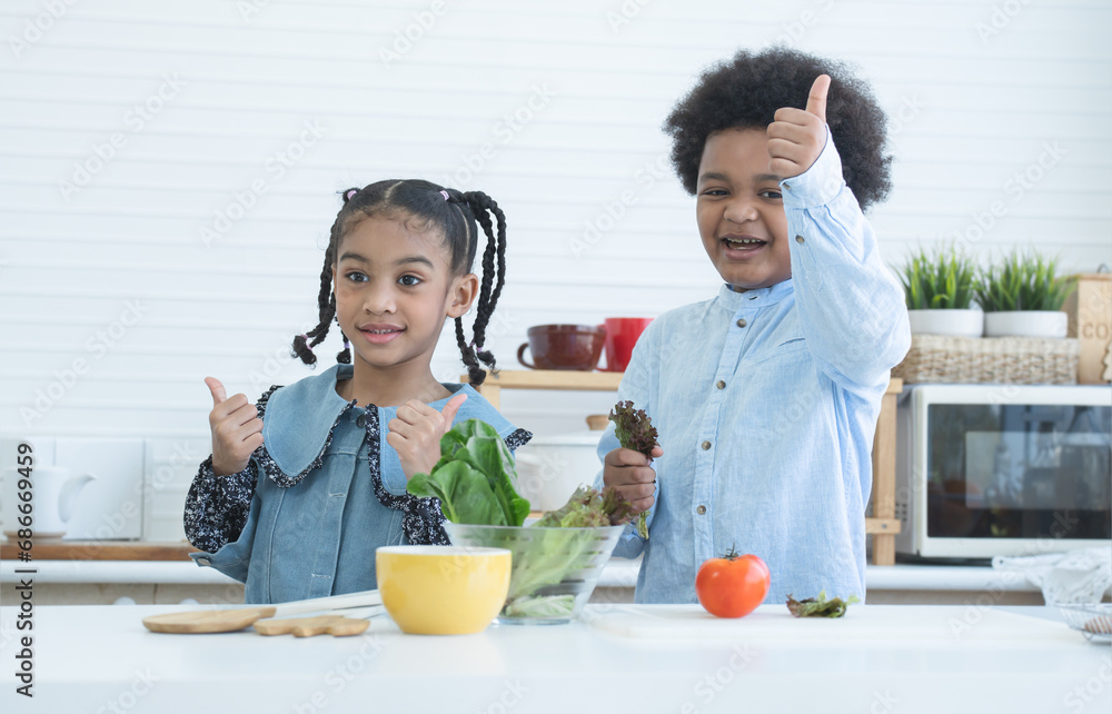 Two African cute sister and brother smiling, thumbs up cheering for eat fresh vegetables at home kitchen. Boy holding green salad vegetable in hand. Healthy food, good for kids Two African cute sister and brother smiling, thumbs up cheering for eat fresh vegetables at home kitchen. Boy holding green salad vegetable in hand. Healthy food, good for kids