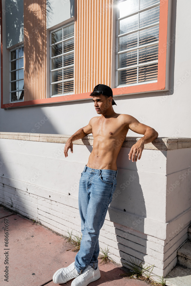 Sexy shirtless cuban man with athletic body in baseball cap and jeans