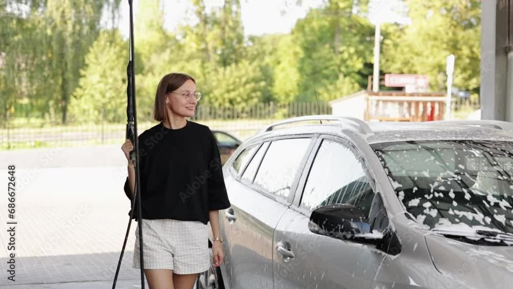 Smiling young attractive woman having fun with car washer gun, using like shot in camera. Girl is washing her vehicle at a self-service car wash. Car cleaning tools Smiling young attractive woman having fun with car washer gun, using like shot in camera. Girl is washing her vehicle at a self-service car wash. Car cleaning tools