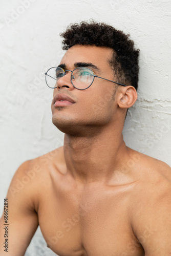 Portrait of shirtless muscular young cuban man with curly hair and stylish round-shaped eyeglasses