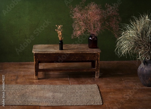 Desktop background. There is a vintage wooden table against the background of a green wall, two vases on the table, and a jug of dried flowers on the floor. Vintage. Renaissance style. Retro still lif photo