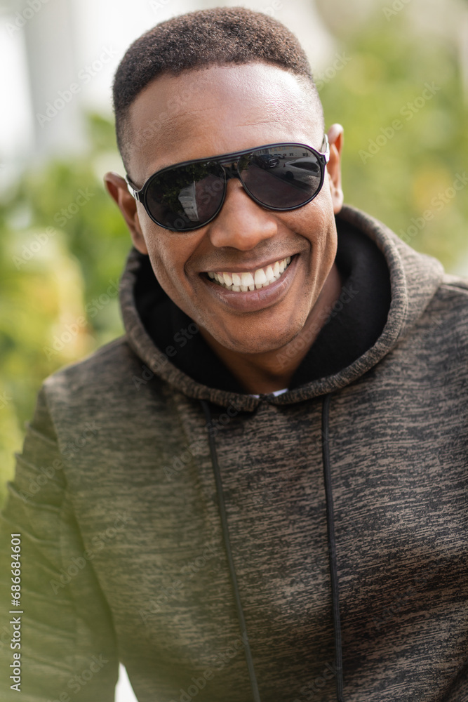 portrait of positive african american man in hoodie and stylish sunglasses smiling outdoors portrait of positive african american man in hoodie and stylish sunglasses smiling outdoors